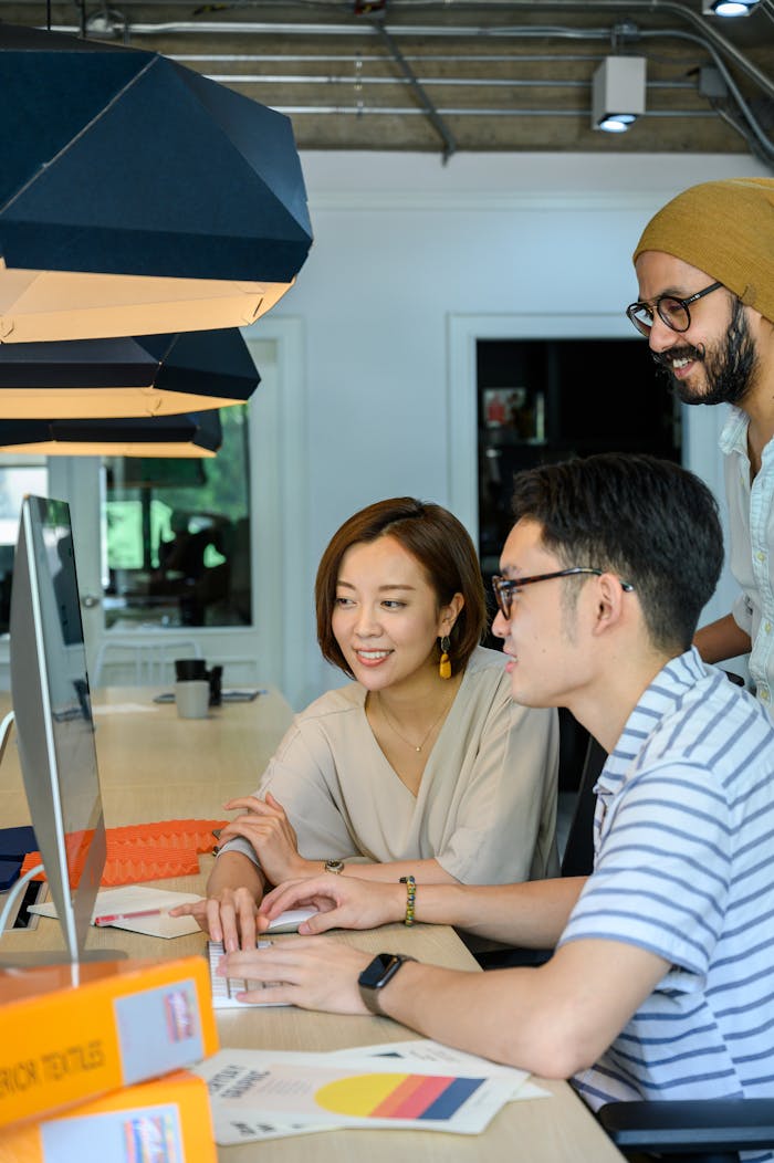 Three adults collaborating at a desk in a modern office setting, working closely together.