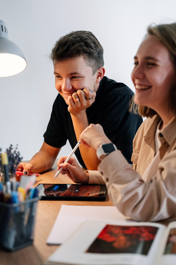 Two young adults smiling and collaborating using a digital tablet with stylus.