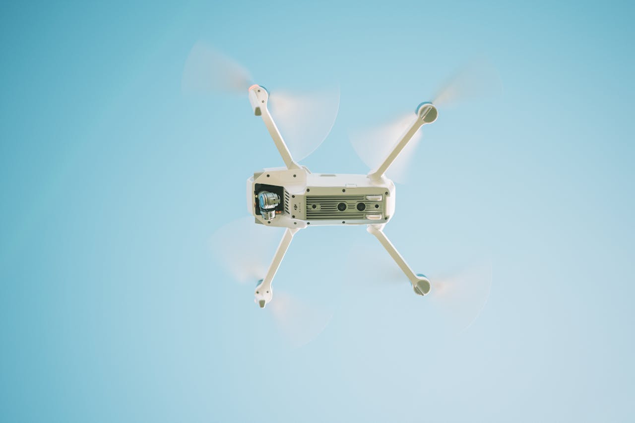 A sleek white drone flying under a clear blue sky, capturing aerial views.